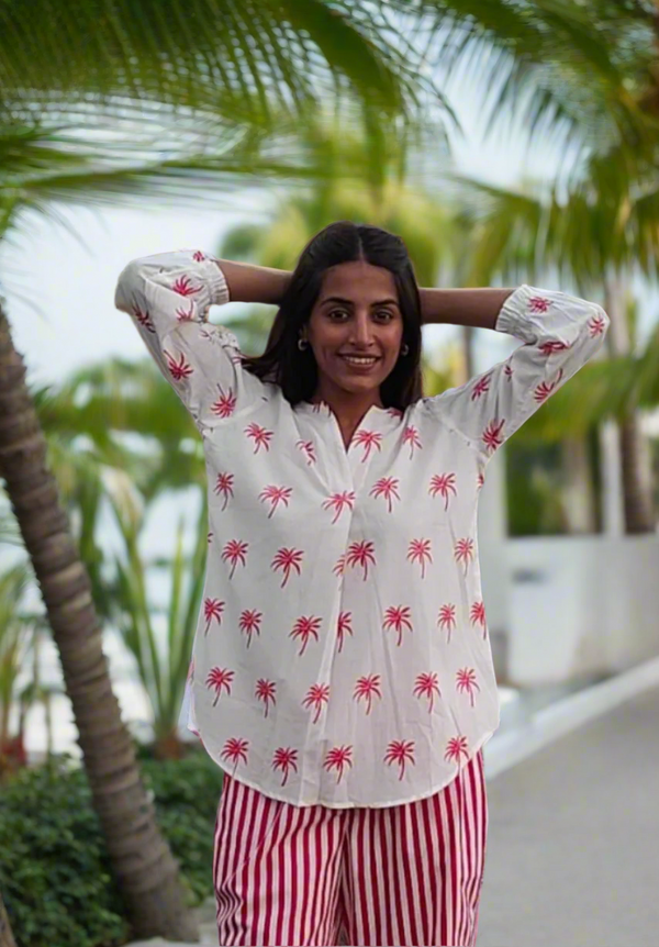 Woman wearing a white shirt with pink palm tree pattern and red striped pants outdoors.