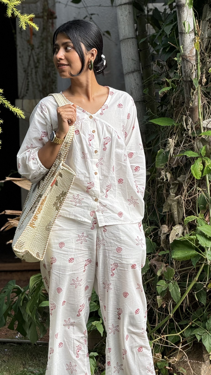 Woman in a white floral outfit holding a bag outdoors with greenery around