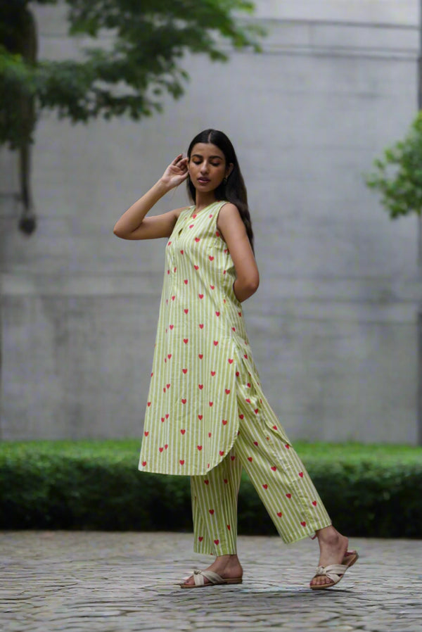 Woman in a light green dress with red patterns standing in front of a red and white wall.